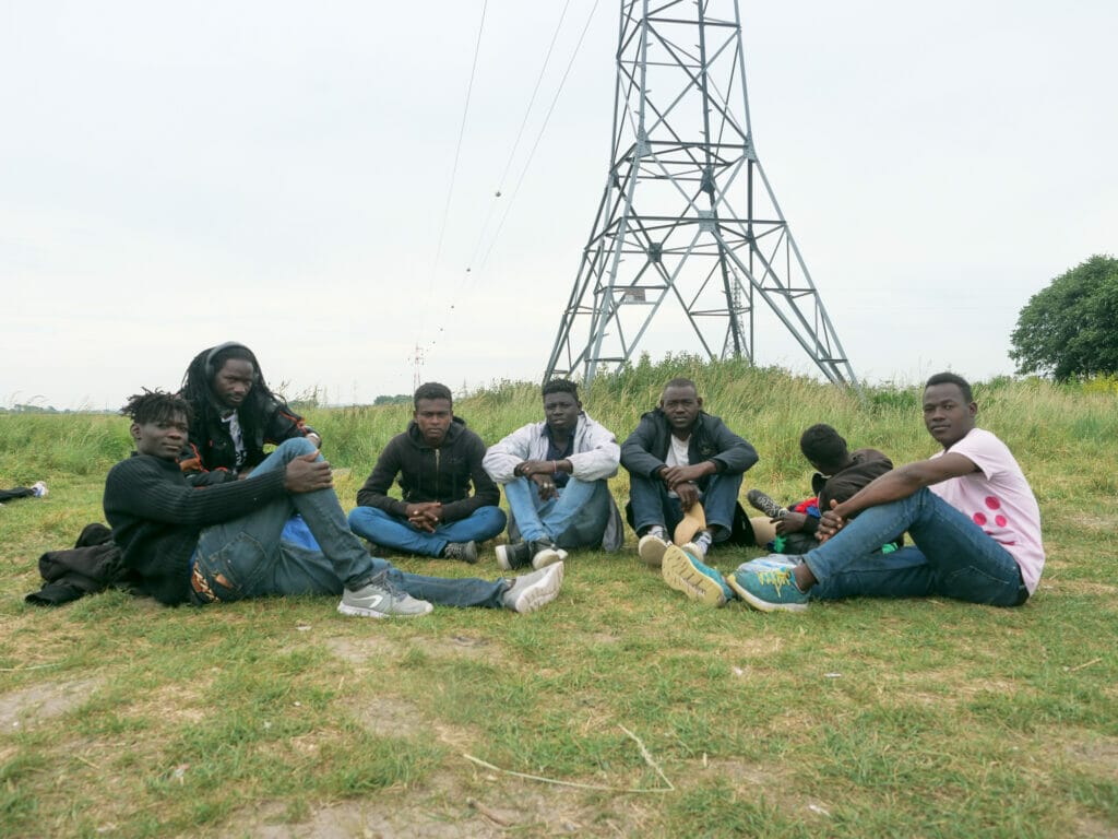 In Calais hoffen Mitte Juni rund 1000 Menschen auf einen Weg Richtung Großbritannien. Eine Gruppe sitzt auf einem Feld.