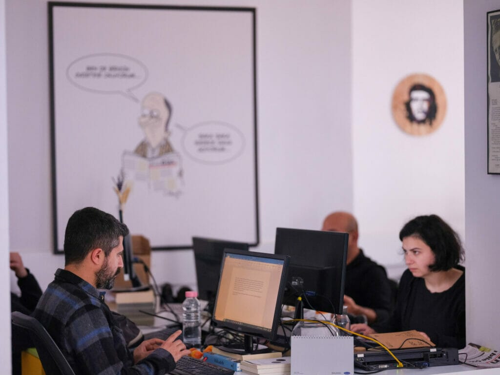 Das Foto zeigt ein Gemeinschaftsbüro der türkischen Tageszeitung BirGün. An zusammengeschobenen Schreibtischen sitzen vier Redakteur:innen und arbeiten. Im Hintergrund hängt eine Karikatur an der Wand und daneben das Konterfei Guevaras.