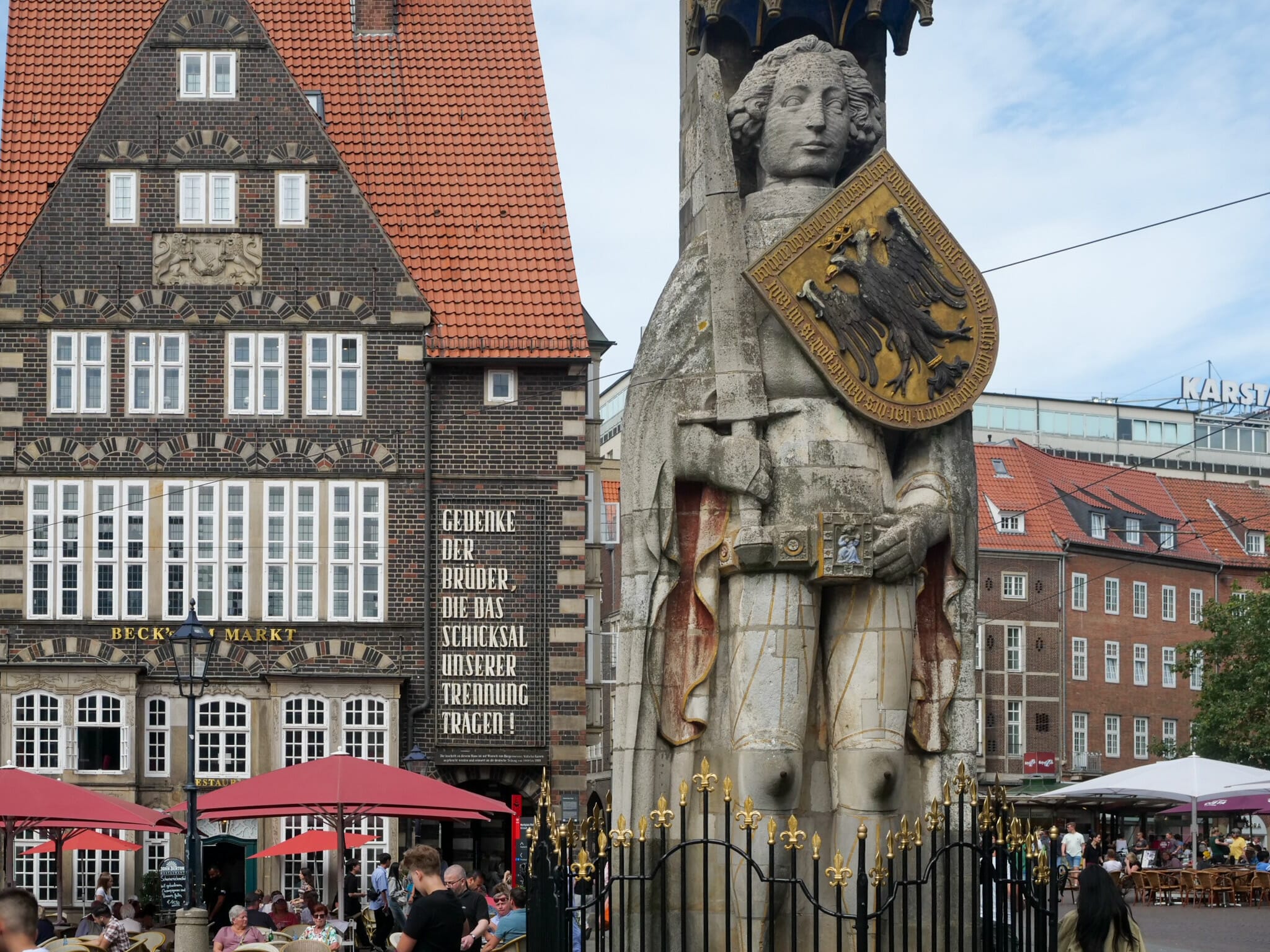 Der Bremer Roland, ein Wahrzeichen der Stadt, auf dem Marktplatz. Dahinter prangt auf einem Haus der Schriftzug „Gedenke der Brüder, die das Schicksal unserer Teilung tragen“.