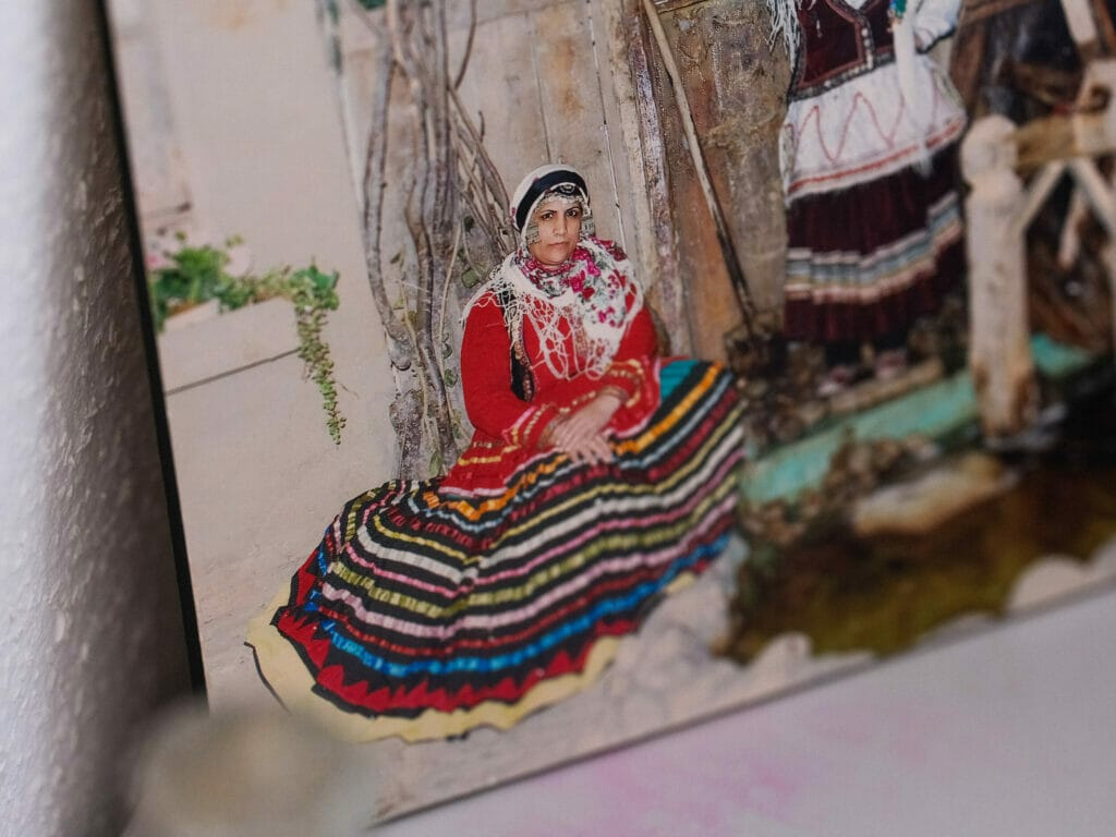 A photo that almost looks like a painting: it shows a woman in traditional dress sitting on the floor, her top is red, the skirt spread out with many color rings.
