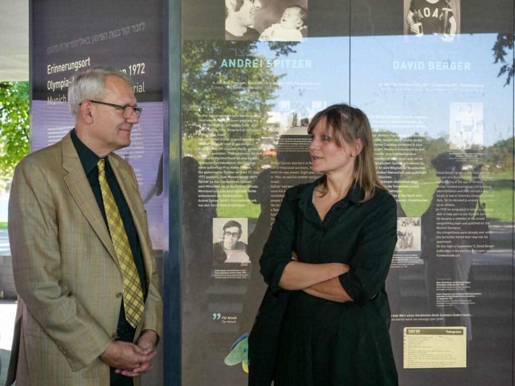 Ein Mann und eine Frau unterhalten sich vor einer Gedenktafel.