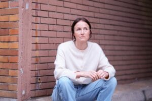 Marie-Kristin Thiele sitzt in Jeans und weißem Pullover vor einer Ziegelwand.