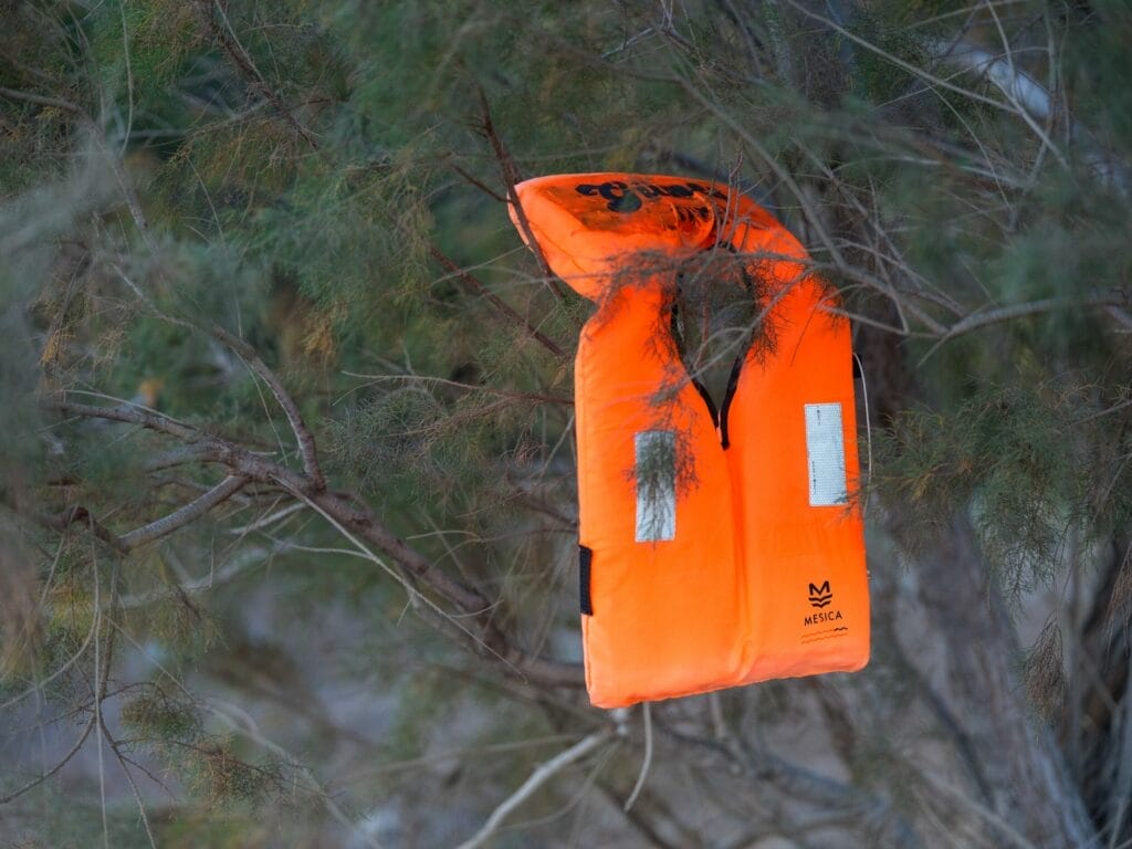 Eine orangefarbene Schwimmweste hängt an einem Baum.