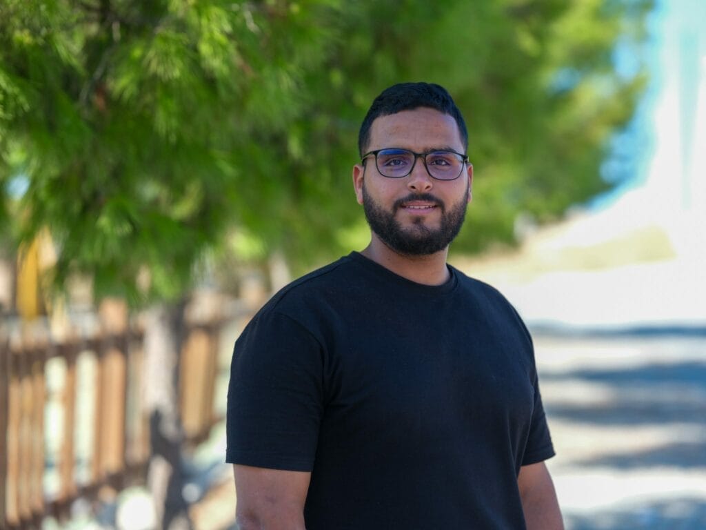 رجل يرتدي نظارة وقميصا أسود يقف أمام شجرة.