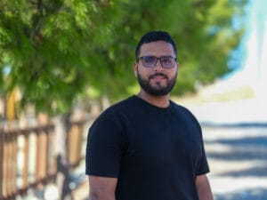 رجل يرتدي نظارة وقميصا أسود يقف أمام شجرة.