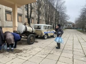 Ein Mann mit Plastiktüten steht auf einem Bürgersteig neben einem Anhänger.