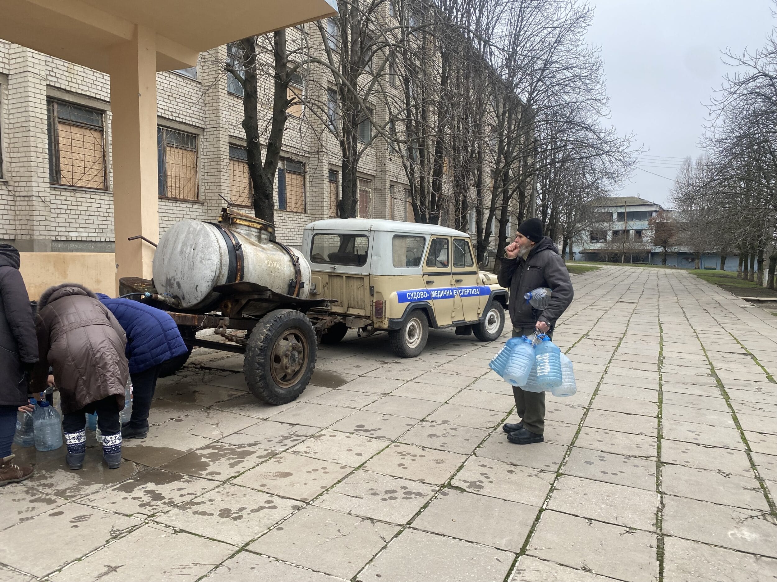 Ein Mann mit Plastiktüten steht auf einem Bürgersteig neben einem Anhänger.