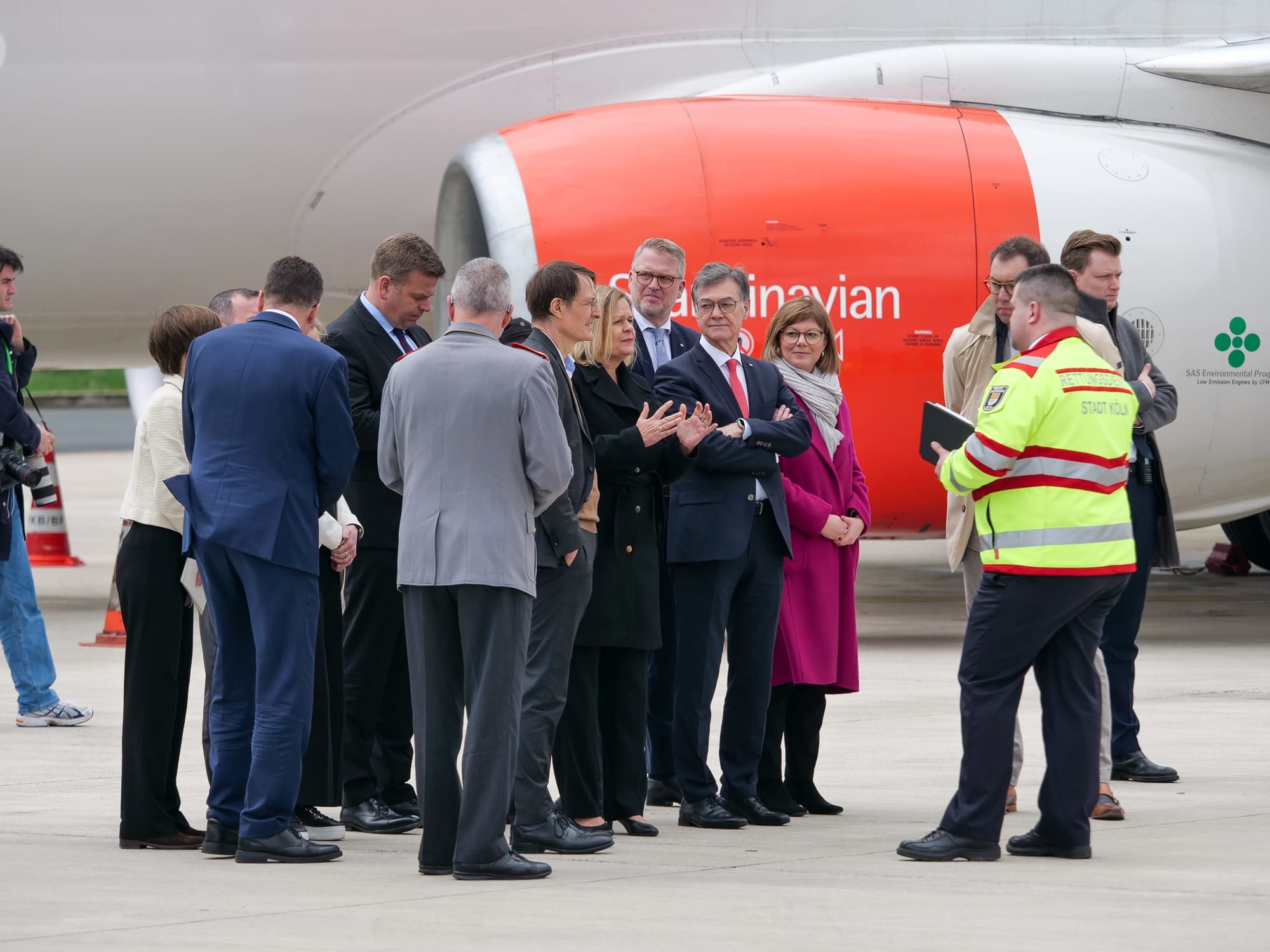 Eine Gruppe von Personen in Berufskleidung diskutiert auf dem Rollfeld eines Flughafens neben einem Flugzeug.