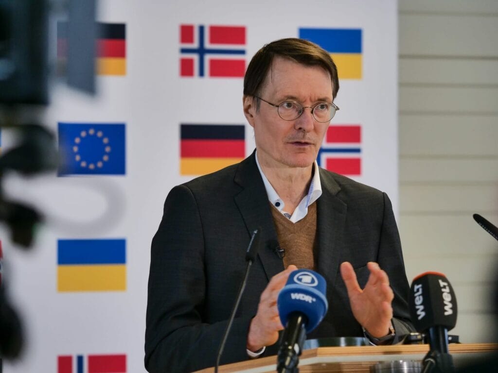 Ein Mann spricht auf einer Pressekonferenz mit Nationalflaggen und Flaggen der Europäischen Union im Hintergrund.