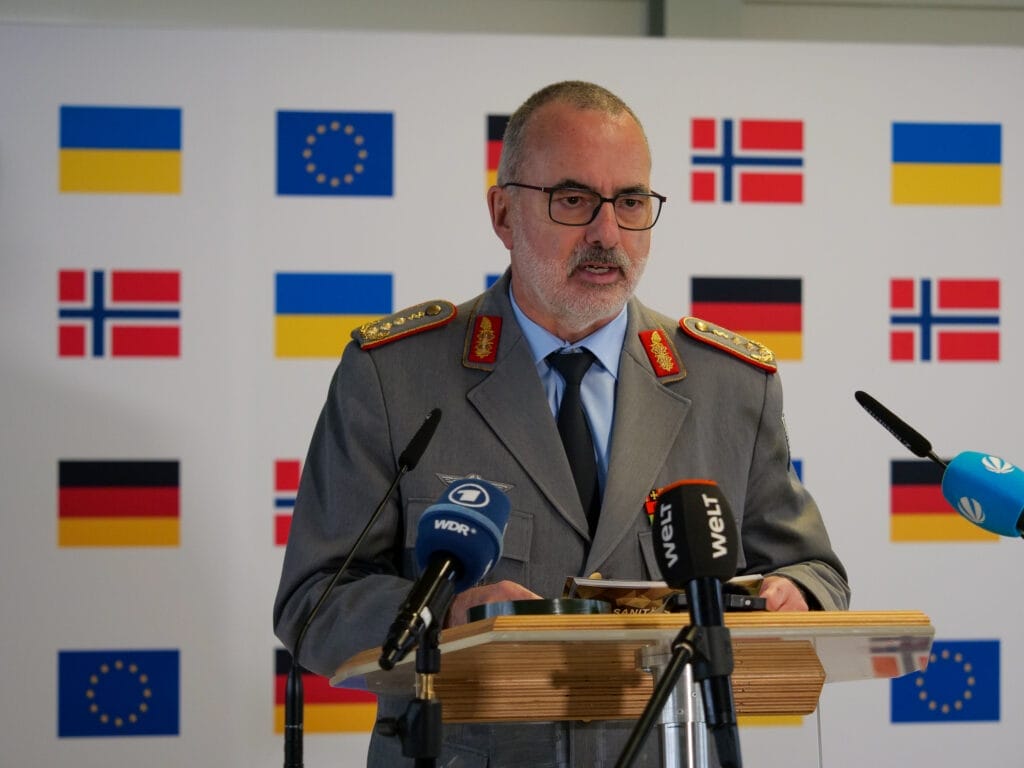 Ein Militäroffizier hält eine Rede auf einem Podium mit europäischen Flaggen im Hintergrund.