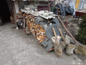Ein provisorischer Brennholzunterstand mit Wellblechdach und einem Stapel gehacktem Holz.
