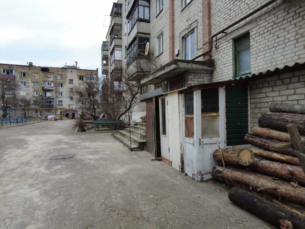 Ein Wohngebiet mit einem alten Gebäude und gestapelten Baumstämmen im Vordergrund.