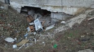 Beschädigtes Gebäude mit eingestürzter Wand und Trümmern, darunter Haushaltsgeräte.