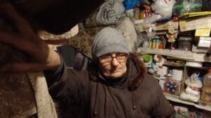 Eine Person mit Strickmütze und Brille in einem vollgestopften Raum.