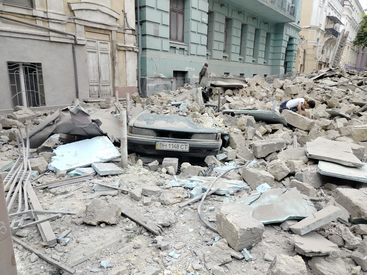 A car buried in rubble amidst a scene of urban destruction.