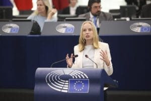 Eine Frau spricht an einem Podium im Europäischen Parlament. Zu sehen sind die blau-weißen EU-Symbole. Hinter ihr sitzen Zuhörer.